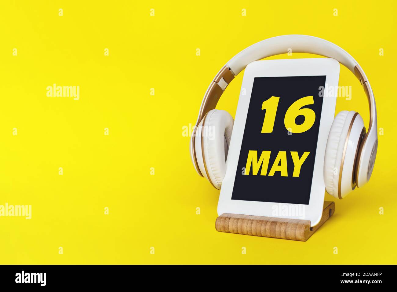 16 de mayo. Día 16 del mes, fecha del calendario. Auriculares elegantes y tableta moderna sobre fondo amarillo. Espacio para texto. Concepto de educación, tecnología, li Foto de stock