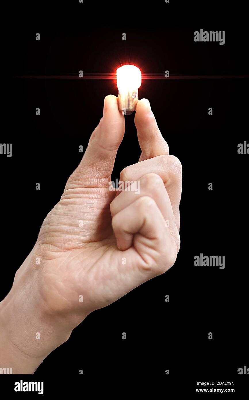 La mano de un hombre sostiene una pequeña bombilla brillante en sus dedos. Aísle sobre un fondo negro. En blanco para el diseño Foto de stock