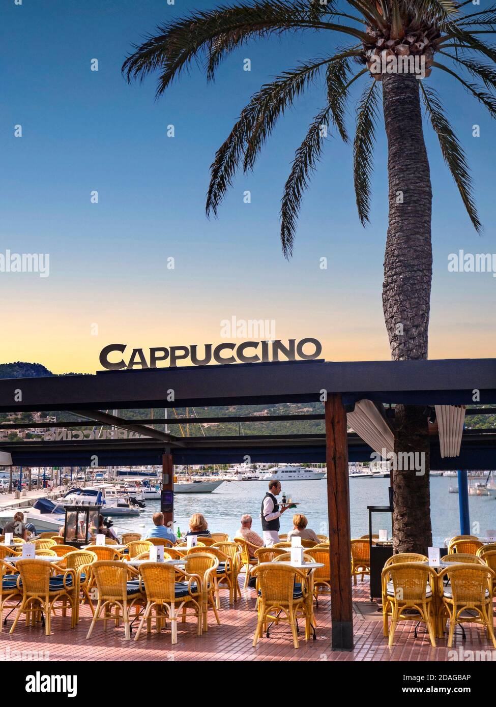 PORT ANDRATX Mallorca Alfresco Café Restaurante Cappuccino Al atardecer, un  camarero tradicional que sirve refrescos en mesas de lujo junto al mar, con  una típica palmera en Puerto Andratx MALLORCA España Islas