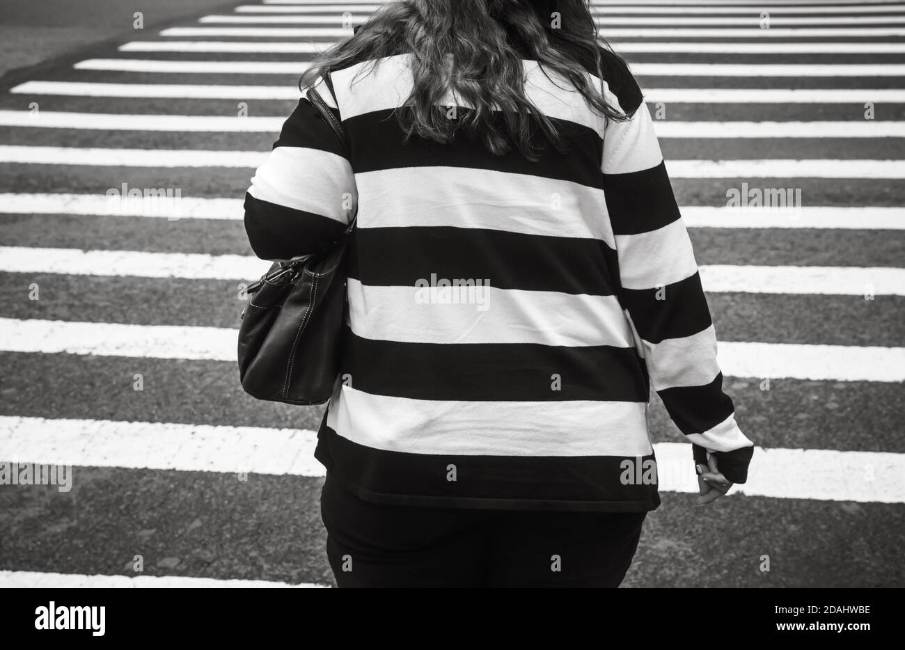 retrasar sensibilidad Tren Escena callejera de Manhattan en blanco y negro. Una mujer gorda con suéter  a rayas blancas y negras cruza la calle en un cruce peatonal en New Yo  Fotografía de stock -