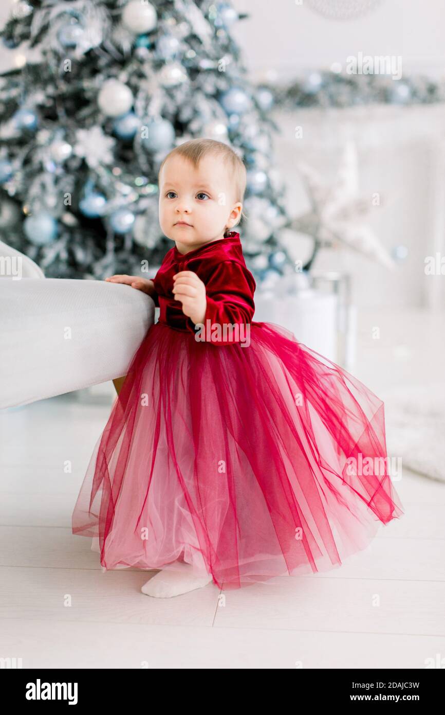 Lindo bebé niña con vestido rojo de pie cerca de la silla en el fondo de  hermoso árbol de Navidad y decoraciones. Navidad, familia, año Nuevo  Fotografía de stock - Alamy