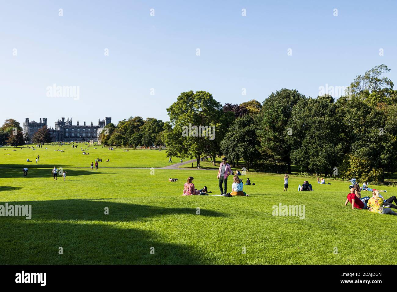 Gente disfrutando del tiempo soleado en la hierba en los terrenos del castillo de Kilkenny, Condado de Kilkenny, Irlanda Foto de stock