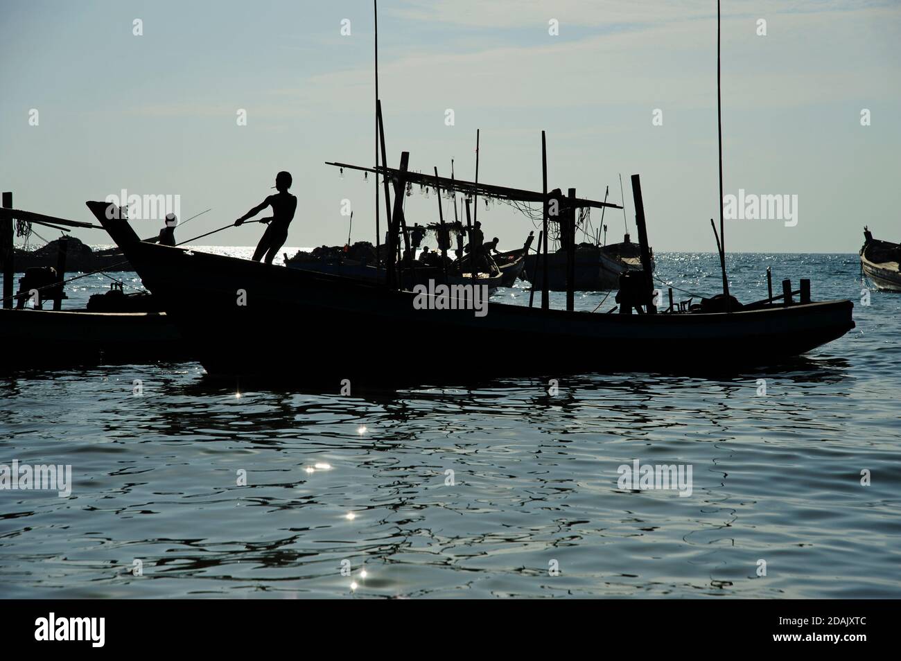 Siluetas de los pescadores birmanos preparan sus barcos de pesca para un Pesca nocturna mientras el sol cae en la playa Ngapali Myanmar Foto de stock