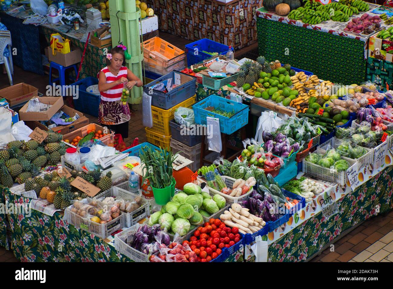 Una dama en su puesto de frutas y verduras locales y tropicales en el mercado de Papeete, Tahití, Polinesia Francesa Foto de stock
