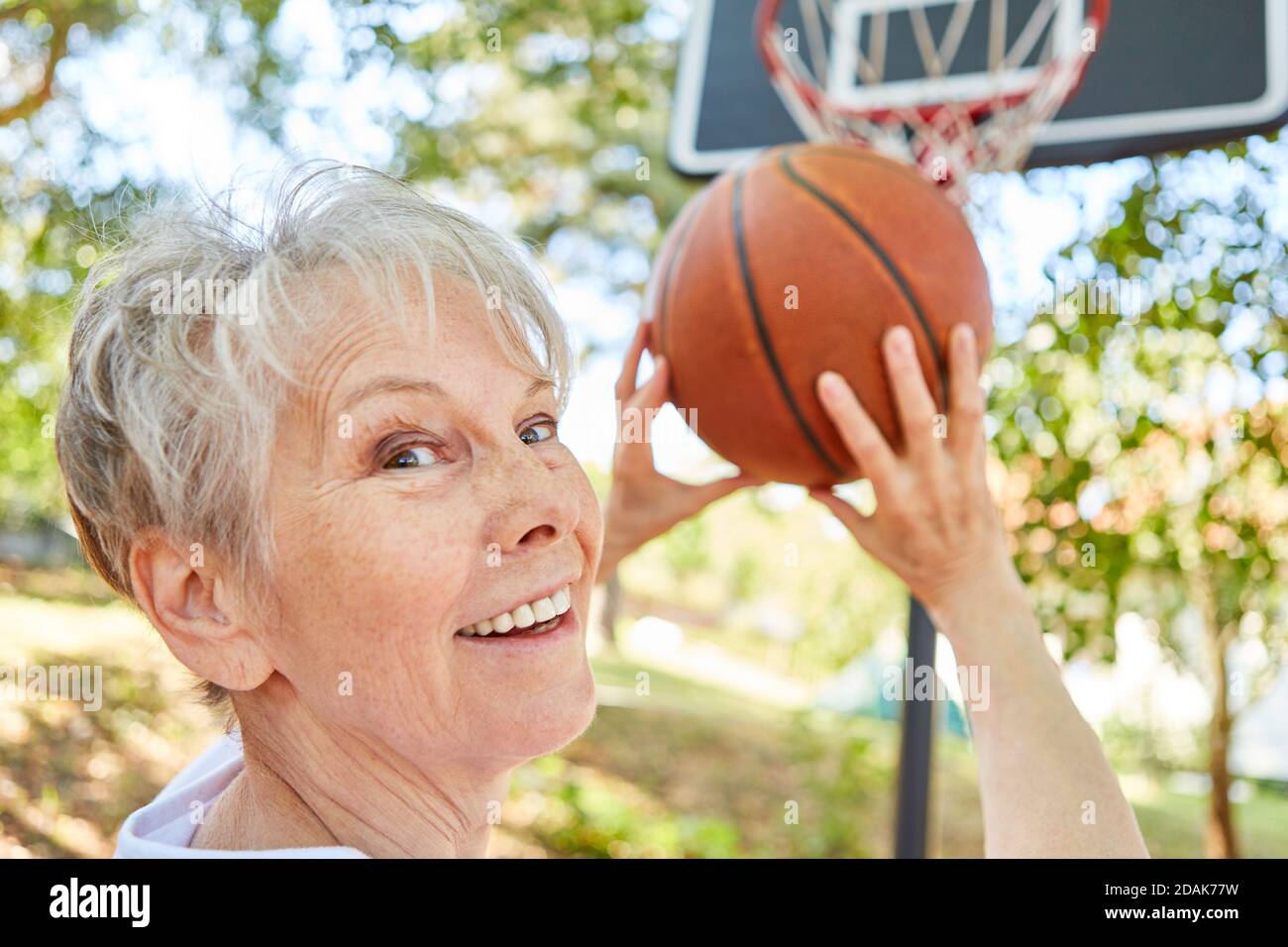 Sonriendo como un ciudadano mayor deportivo y vital pensionista jugando baloncesto en el jardín Foto de stock