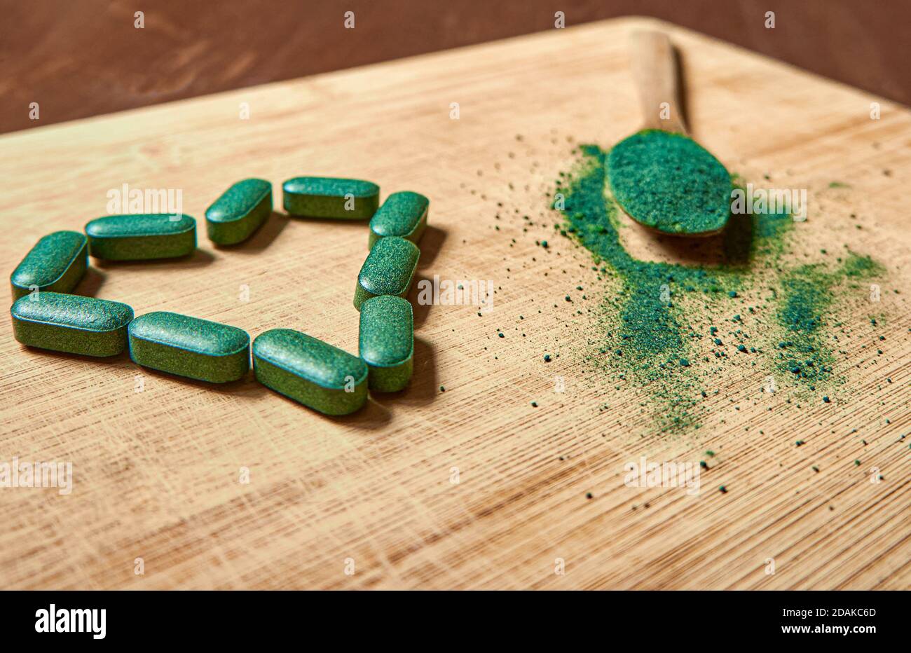 Tabletas de clorela o espirulina en forma de corazón y polvo en una cuchara de madera sobre un fondo de madera clara. Suplemento nutricional, superalimento detox. Foto de stock