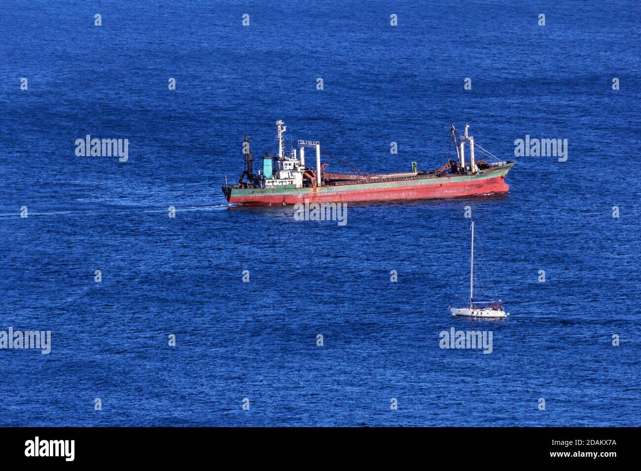 Barcaza de carga y pequeño yate en el mar azul en el día Foto de stock