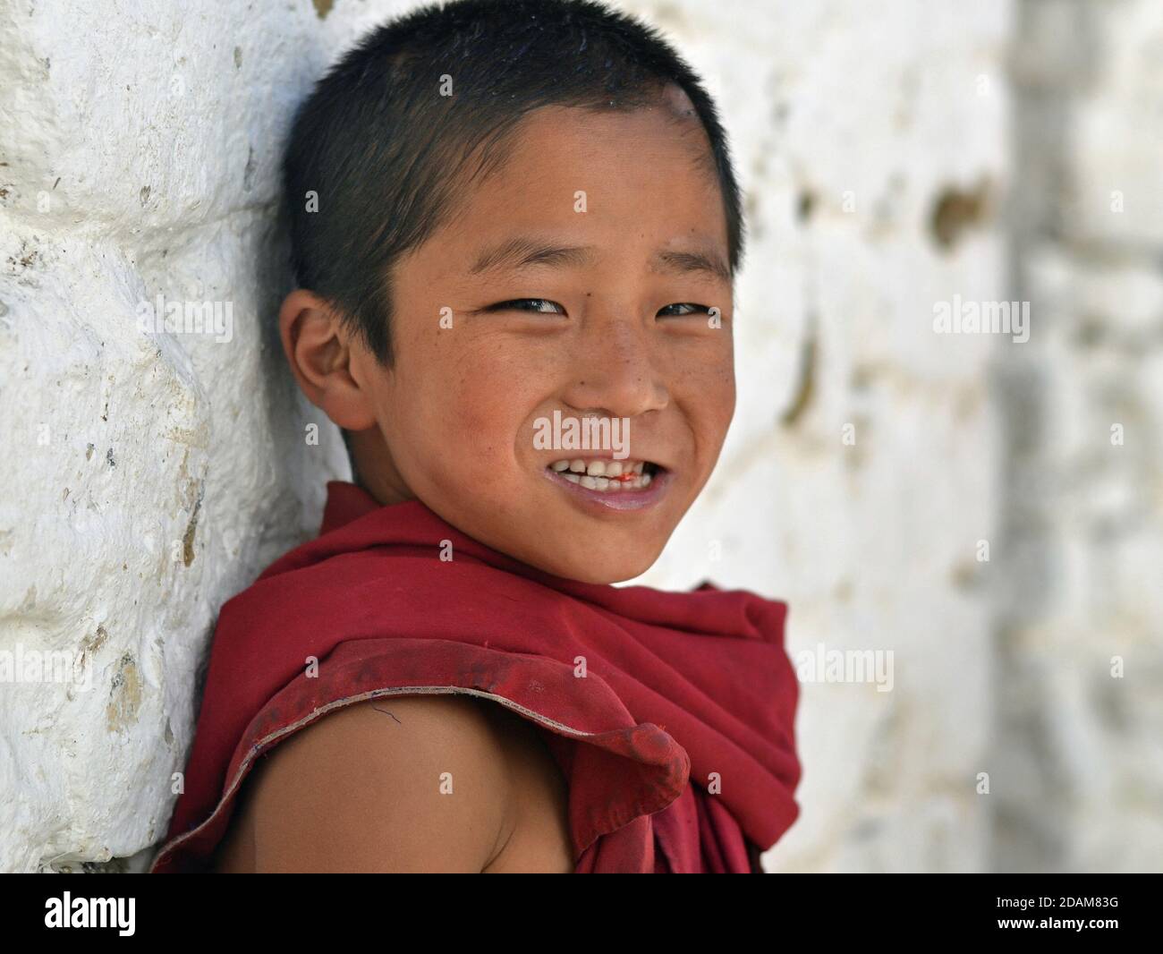 Lindo pequeño monje budista tibetano en bata de granate sonríe para la cámara dentro del monasterio de Tawang. Foto de stock