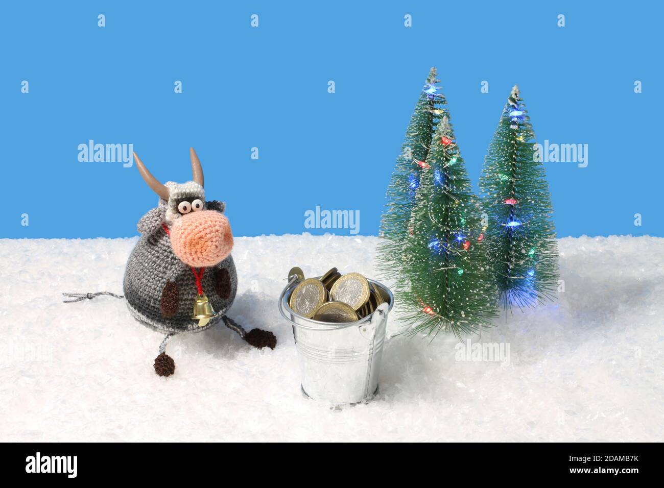 El juguete de lana de punto toro sentado junto al juguete Árboles de  Navidad verdes con luces y cubo de juguete con monedas sobre nieve blanca  artificial contra azur ba Fotografía de