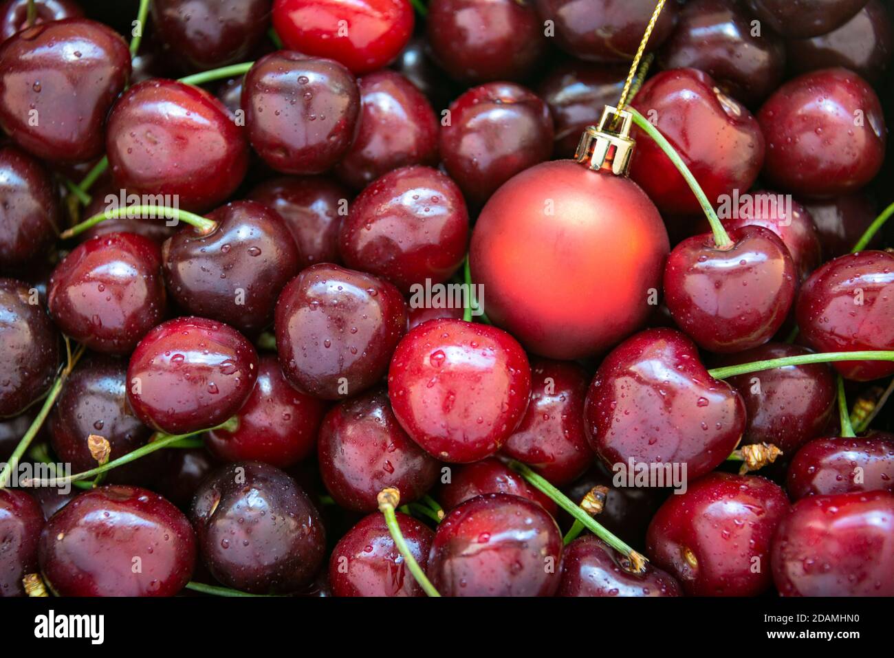 Una bola de Navidad roja entre cerezas rojas maduras, horizontal Foto de stock