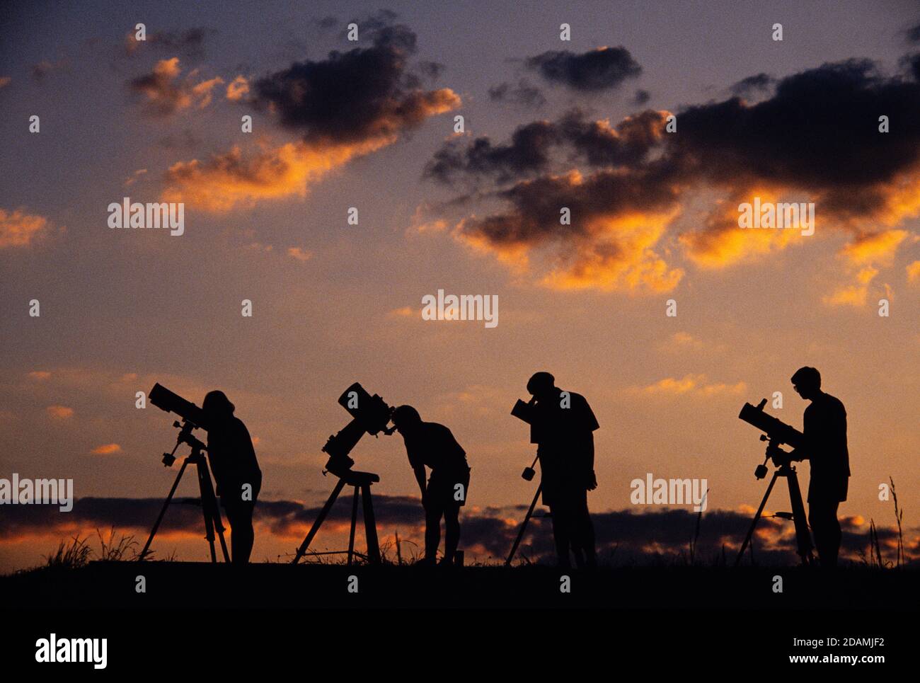 Estudiantes aficionados de astronomía en una colina al atardecer. Foto de stock