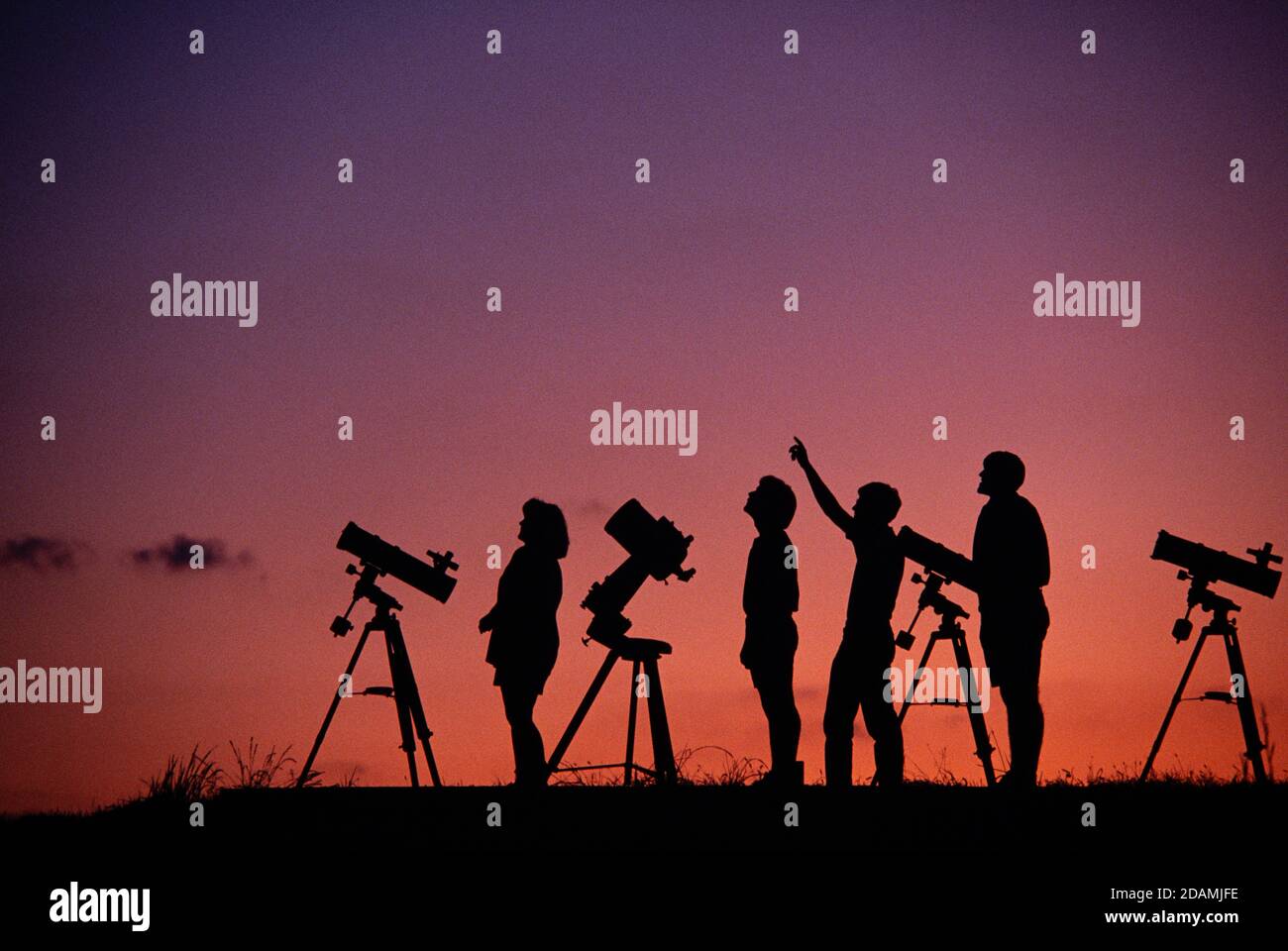 Estudiantes aficionados de astronomía en una colina al atardecer. Foto de stock