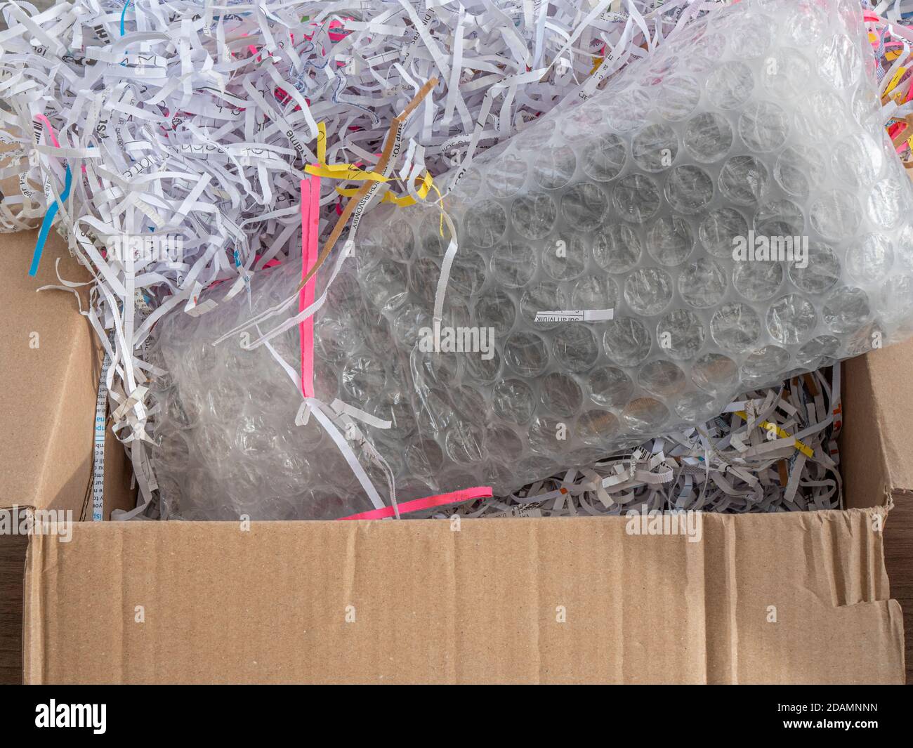 Primer plano PDV de un paquete envuelto en una burbuja en una caja de cartón, que está llena de papel triturado de embalaje. Foto de stock
