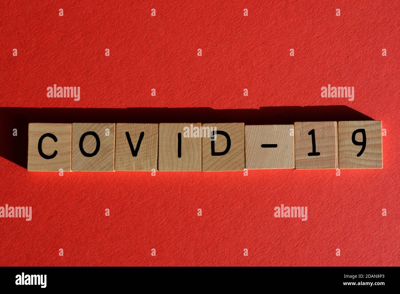 Palabra Covid-19 en letras del alfabeto de madera aisladas sobre fondo rojo Foto de stock