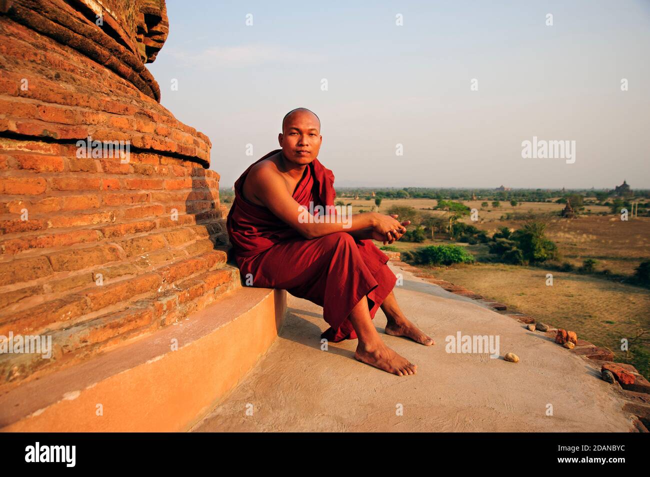 Un joven monje budista en la parte superior de un templo de ladrillo Estructura con el bagan palin detrás de él en Bagan Myanmar Foto de stock