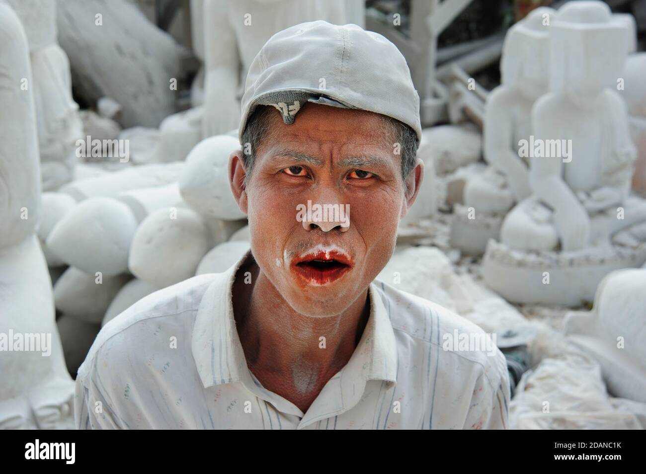 El fantasmal un carver de mármol birmano cubierto de blanco fino polvo de mármol su boca manchada de rojo de la nuez de betel masticando dándole una mirada fantasmal atormentada Foto de stock