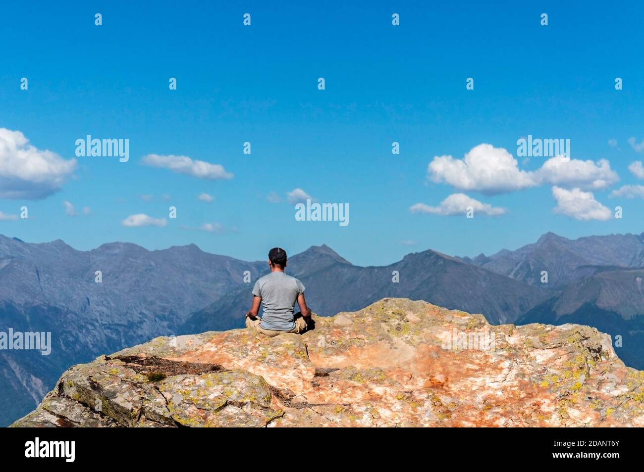 Joven de espalda meditando en roca contra fondo de las montañas del Cáucaso y cielo azul nublado. Relajación en la naturaleza, viajes en solitario, caminata en mountá Foto de stock