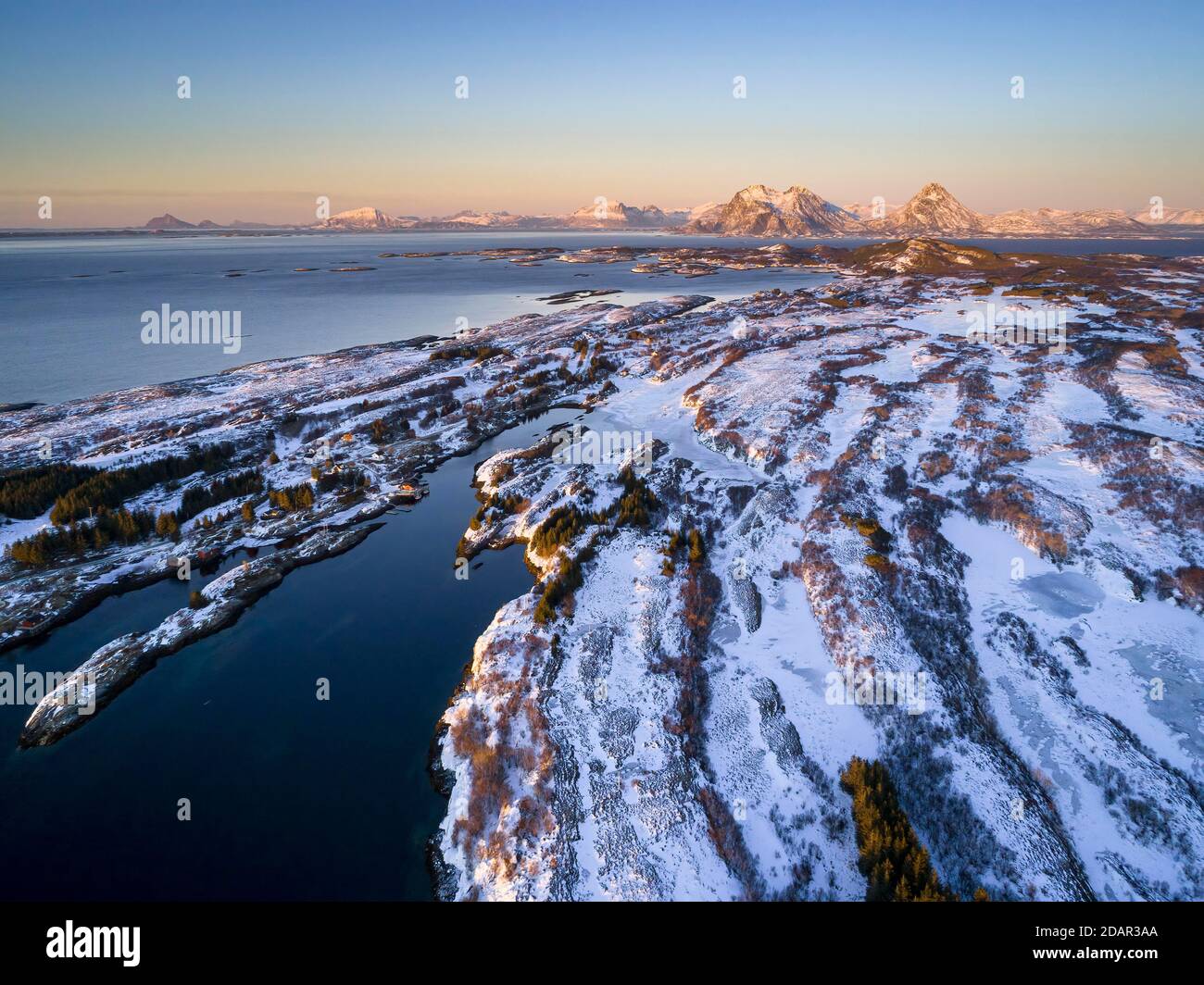 Vista aérea del paisaje de la isla de invierno en la luz de la noche de la costa, altos picos de montaña en el fondo, Donna, Nordland, Noruega Foto de stock