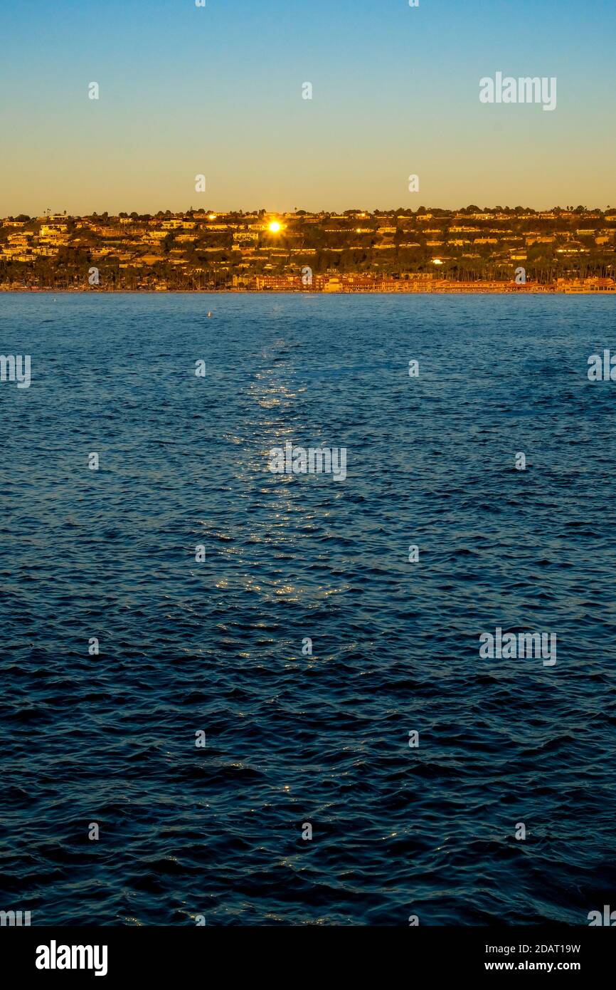 Vista vertical sobre el agua del océano de la Jolla Cove hacia la Jolla Shores San Diego California al atardecer con el sol dorado reflecciónen las ventanas de las casas a Foto de stock