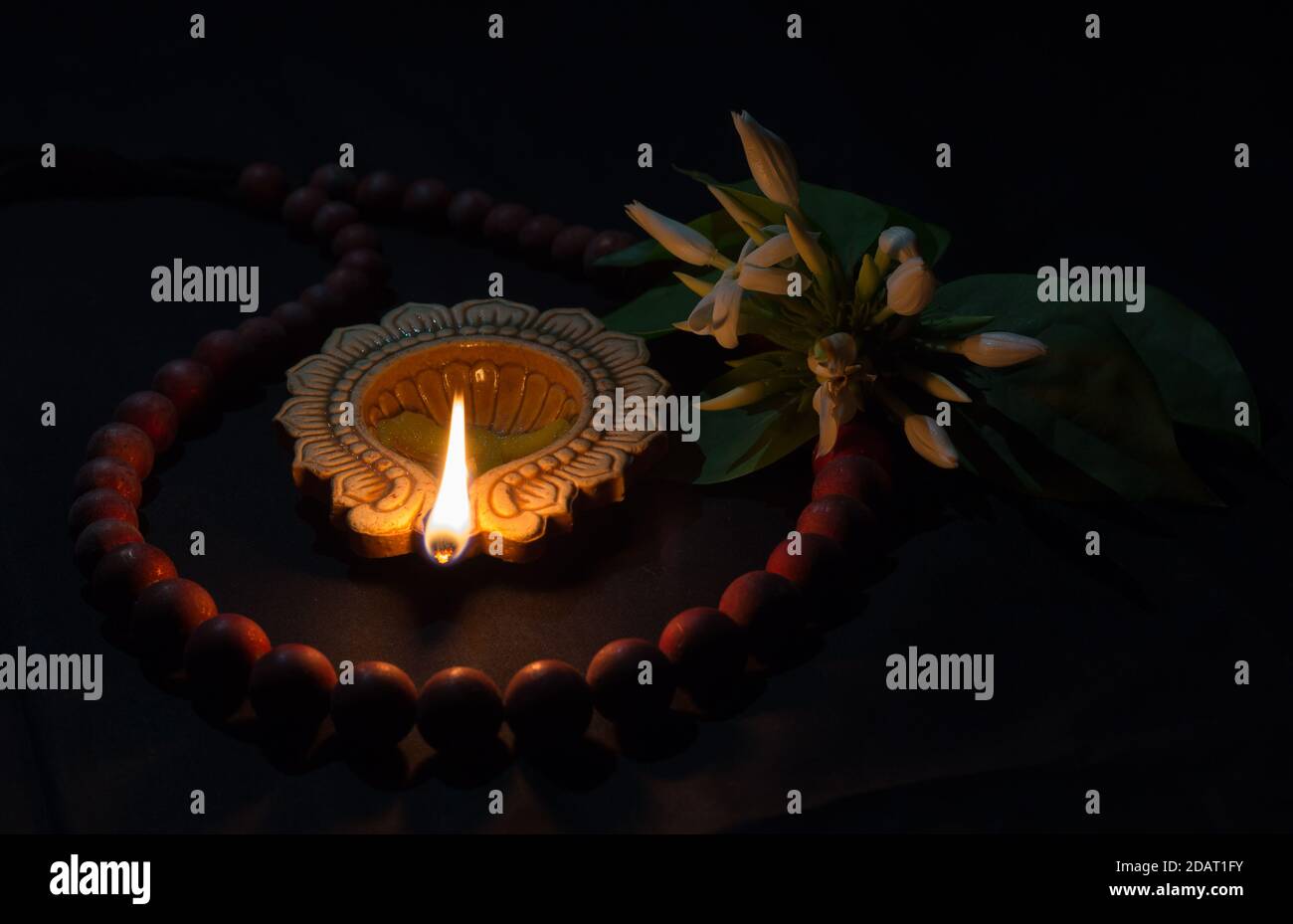 Lámpara de aceite tradicional de la India hecha de arcilla con llama  brillante, flor de jazmín y collar de cuentas de arcilla mantenido sobre  fondo de tela durante la cultura hindú festi