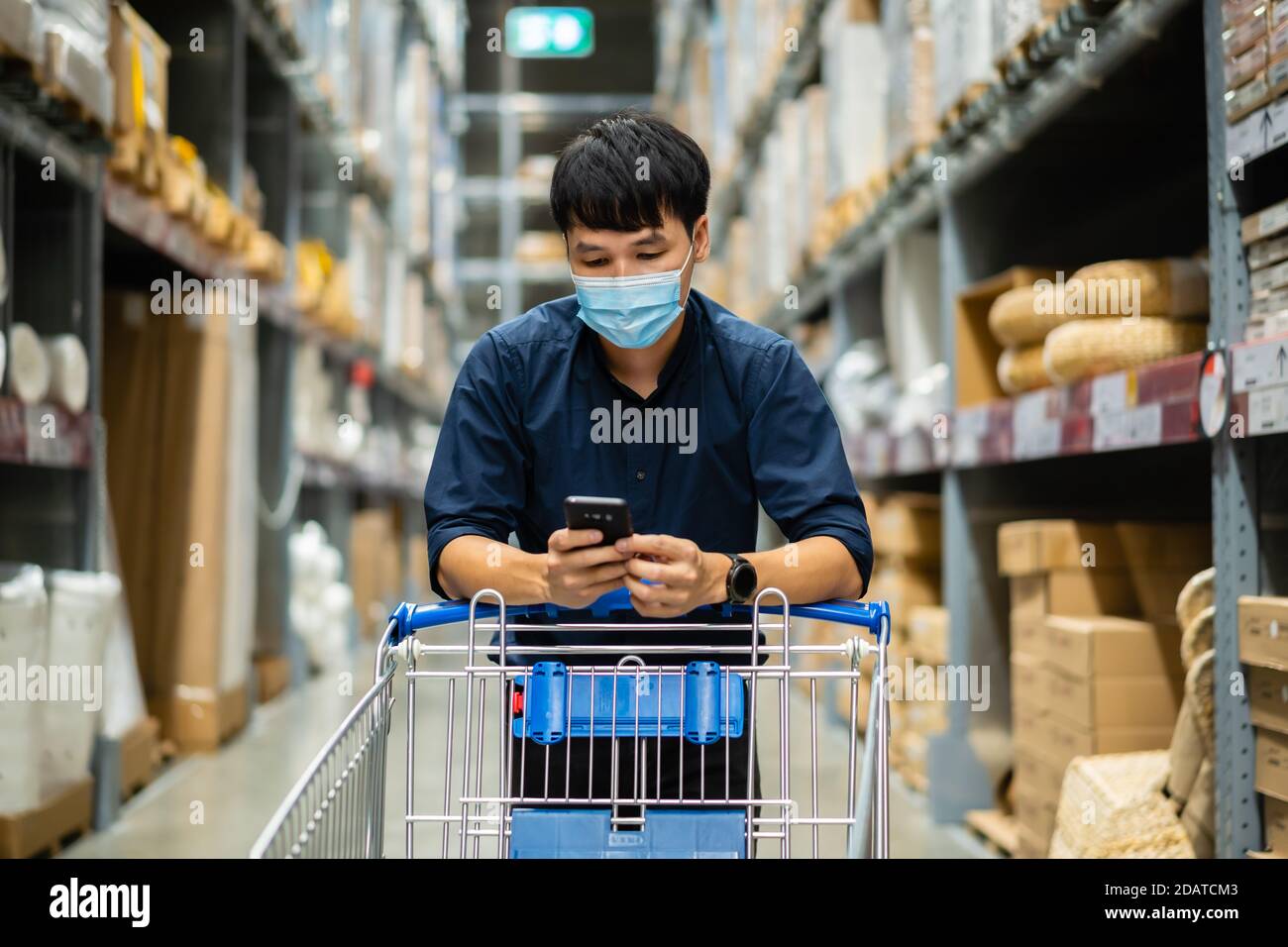 hombre con máscara médica mirando su teléfono móvil y. compras en el almacén durante la pandemia del coronavirus (covid-19) Foto de stock