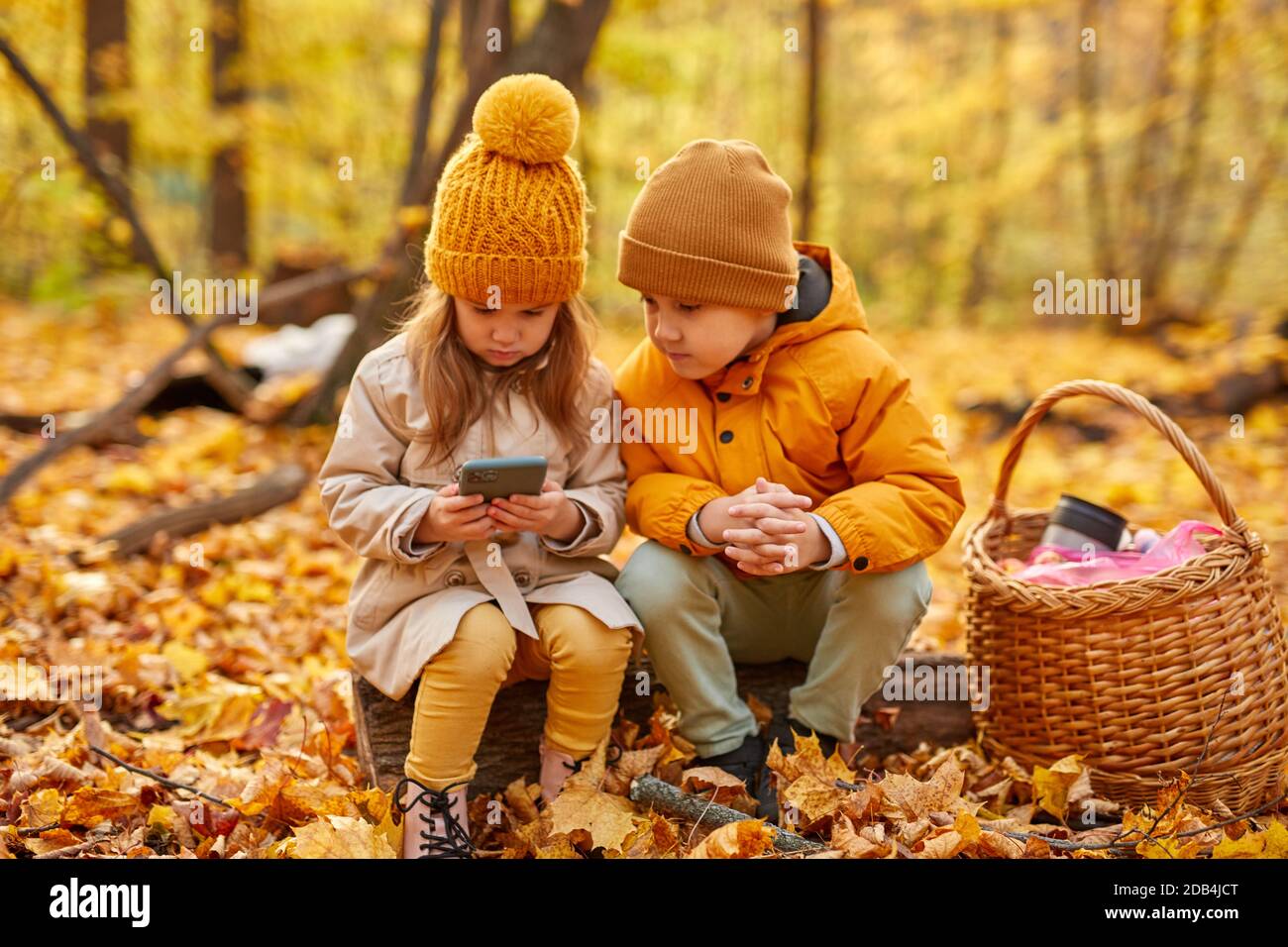 retrato de niños felices pasando tiempo con el teléfono móvil en el bosque, que juegan en el smartphone, en el parque de otoño Foto de stock