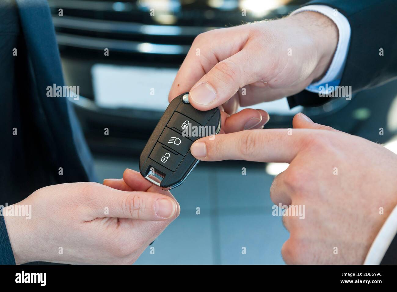 El vendedor de coches entrega las llaves del coche al cliente en el concesionario y explica las funciones Foto de stock