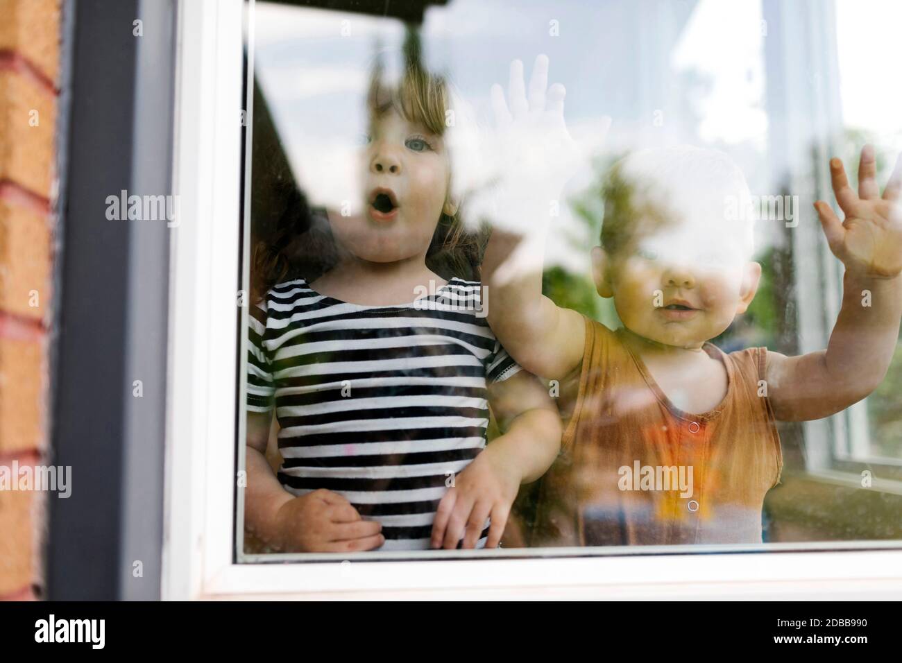 Retrato de niña (2-3) y niño (18-23 meses) de pie detrás de la ventana Foto de stock