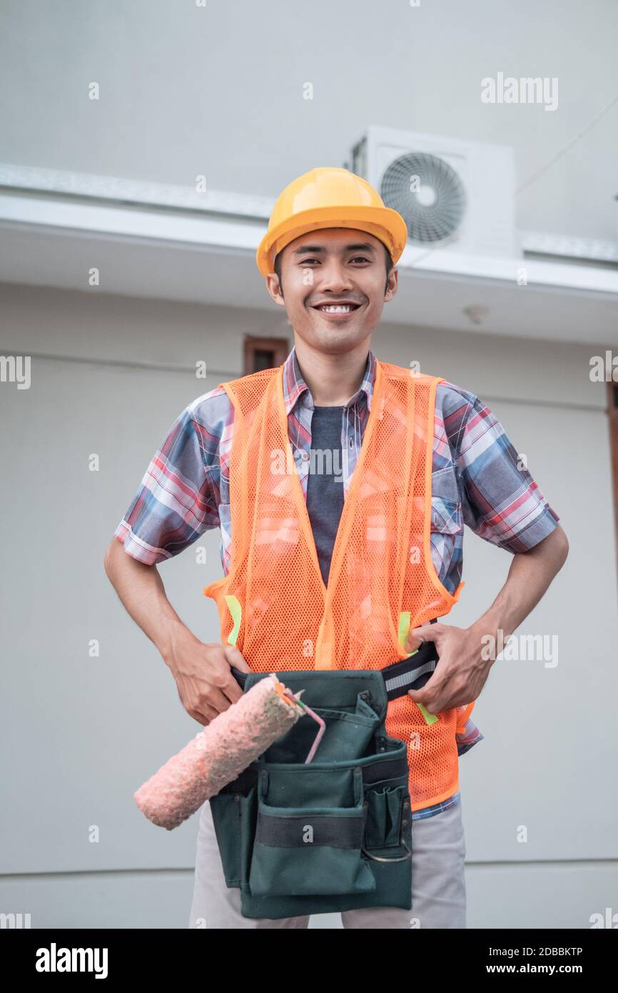 Los trabajadores que usan cascos y chalecos de seguridad mantienen los  rodillos de pintura dentro cinturones de equipo en el fondo de un edificio  de la casa Fotografía de stock - Alamy