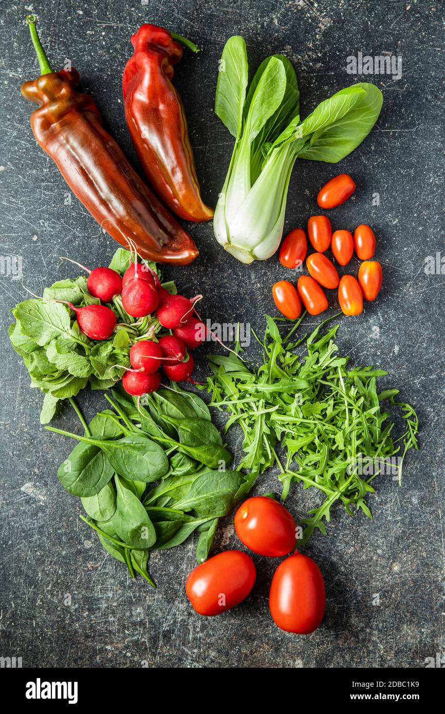 Diferentes verduras. Arúgula, rábanos, espinacas, pimientos rojos, tomates y pak choi en la mesa de la cocina. Vista superior. Foto de stock