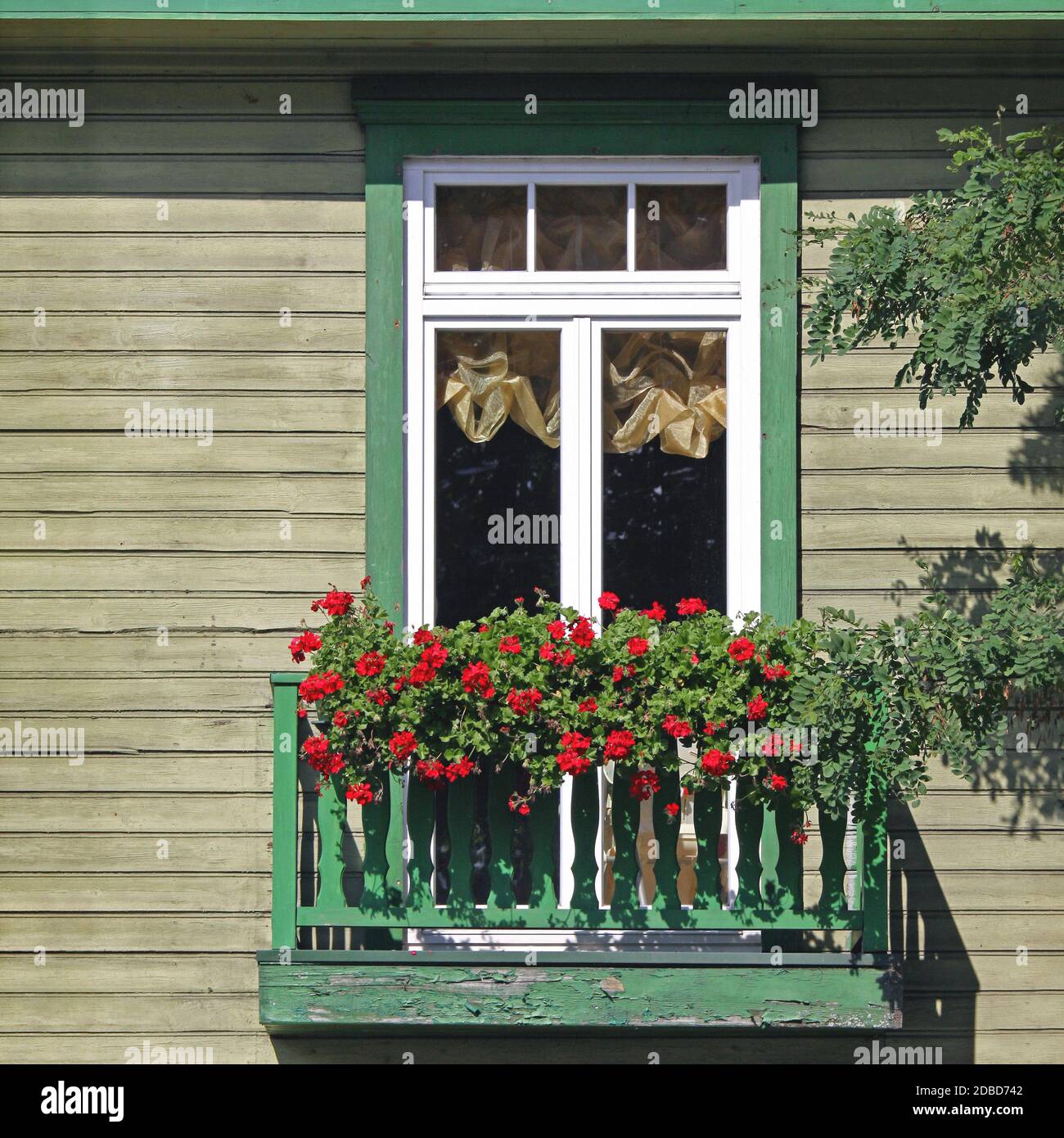 Antiguo balcón de madera con flores rojas en flor en el luminoso día de verano Foto de stock