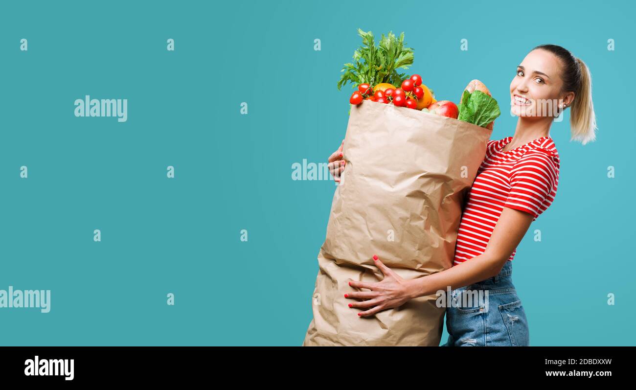 Mujer alegre sosteniendo una enorme bolsa de compras de supermercado llena de verduras frescas, ella está sonriendo con la cámara Foto de stock