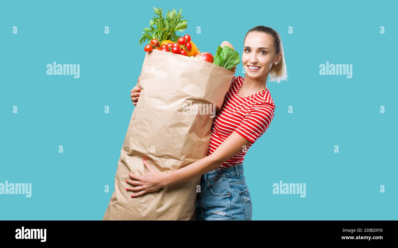 Mujer alegre sosteniendo una enorme bolsa de compras de supermercado llena de verduras frescas, ella está sonriendo con la cámara Foto de stock