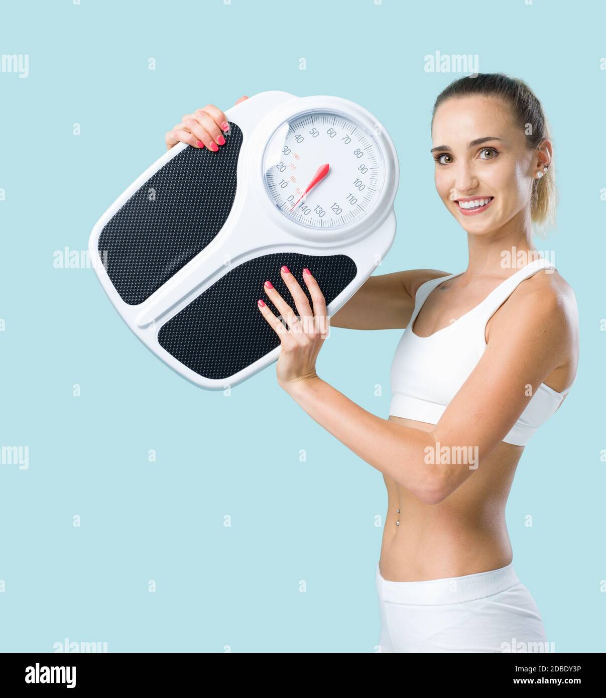 Mujer delgada y sonriente sosteniendo una báscula y mirando la cámara, la pérdida de peso y el concepto de fitness Foto de stock