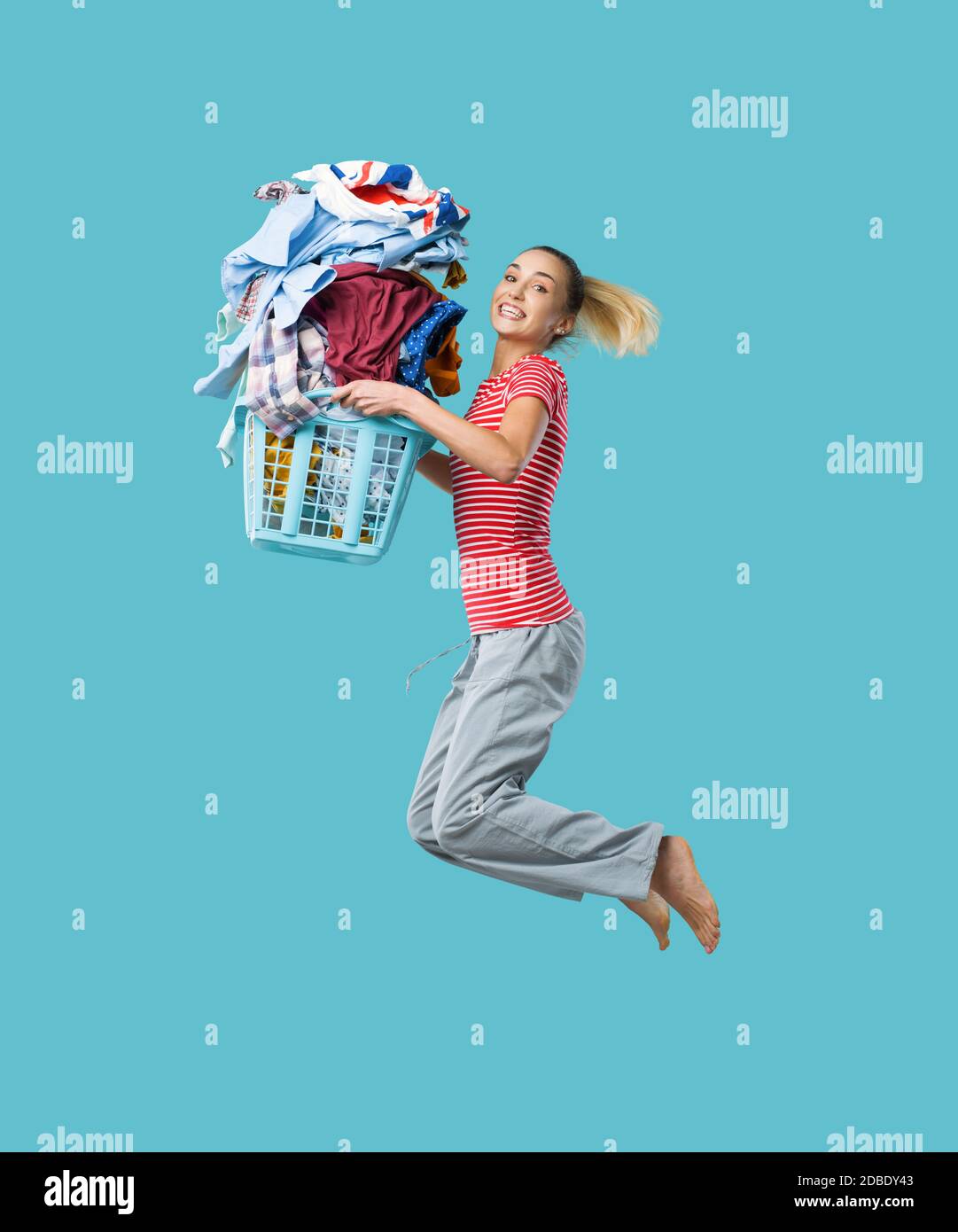 Feliz mujer alegre haciendo la colada y saltando, ella está sosteniendo una cesta de ropa llena de ropa Foto de stock