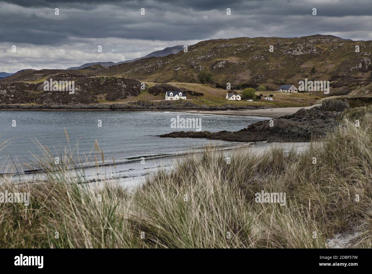 Scottish Highlands West Cove con hierba salvaje y tormentas cielo gris y cabañas en la distancia Foto de stock