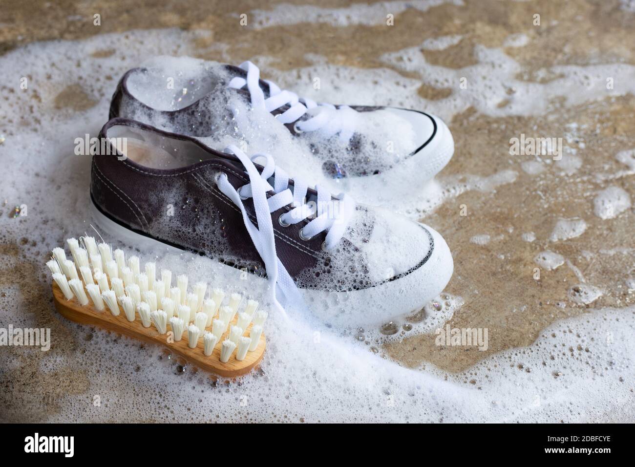 Zapatillas de deporte con espuma de agua detergente en polvo y un cepillo  de madera en el suelo de cemento. Lavar los zapatos sucios Fotografía de  stock - Alamy