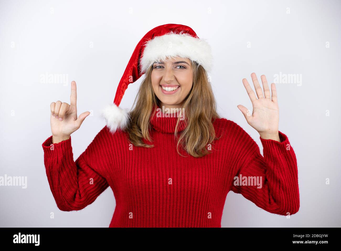 Joven mujer rubia bonita con un suéter informal rojo y un sombrero de  navidad sobre fondo blanco mostrando y apuntando hacia arriba con los dedos  número siete whi Fotografía de stock -