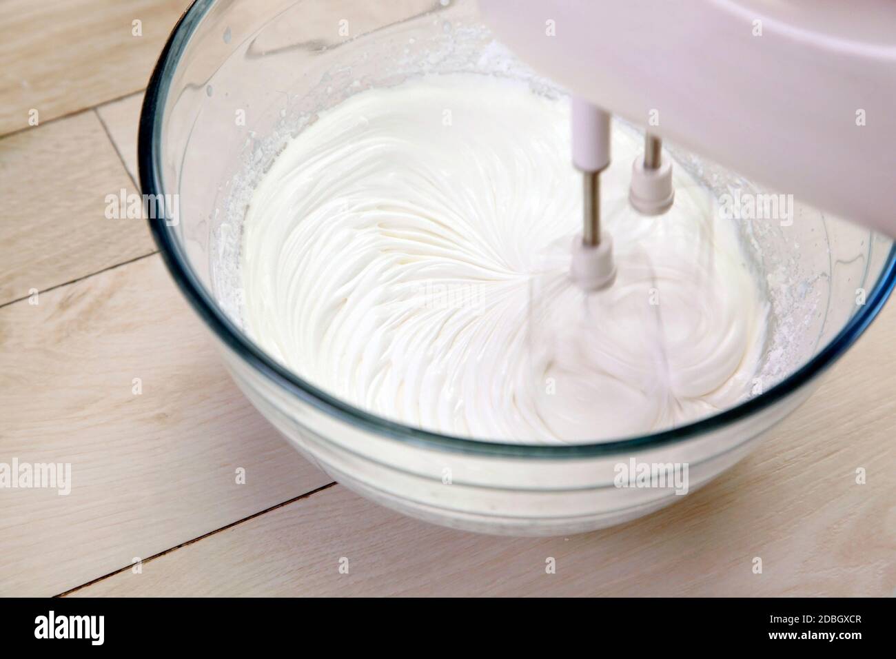 Batido de crema mezcladora en un tazón de vidrio sobre mesa de madera Foto de stock