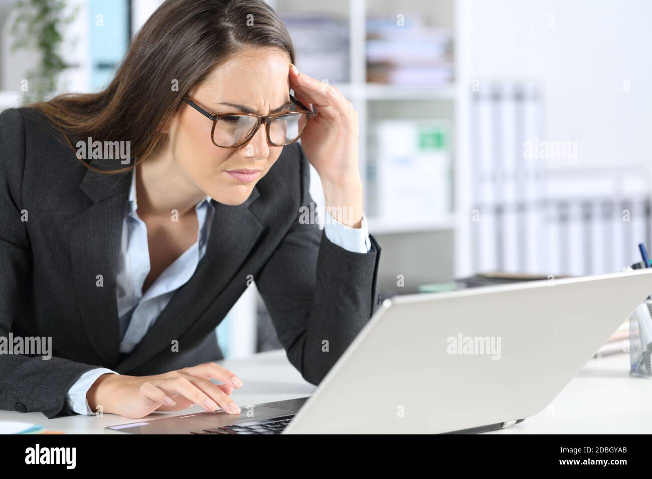Mujer ejecutiva que lleva gafas con problemas de vista tratando de leer en  el portátil sentado en su escritorio en la oficina Fotografía de stock -  Alamy