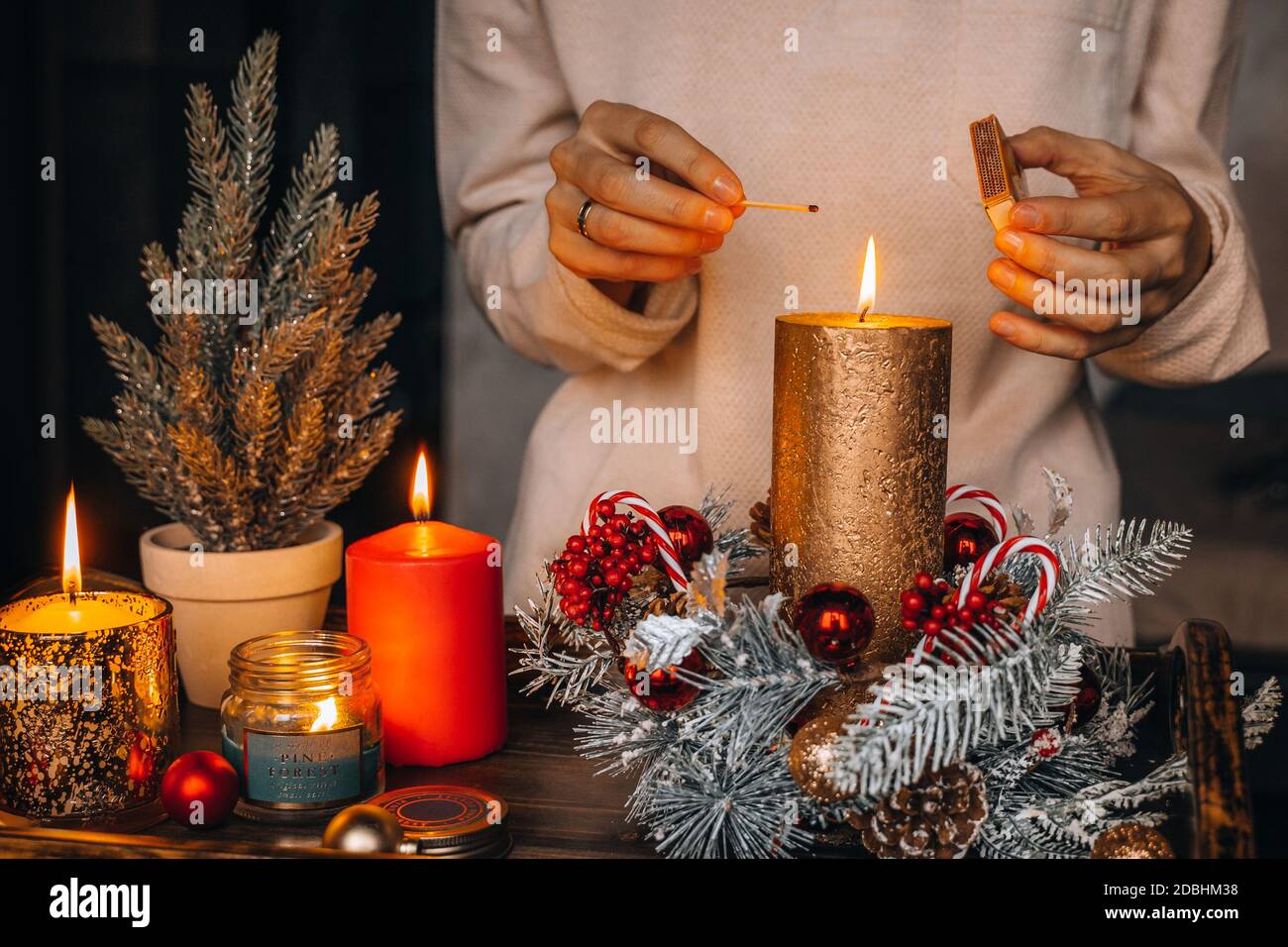 La mujer enciende velas en la mesa decorada en Navidad. Vela de año Nuevo,  tiempo de Adviento, luces cálidas, adornos de decoración de invierno en el  viejo r Fotografía de stock -