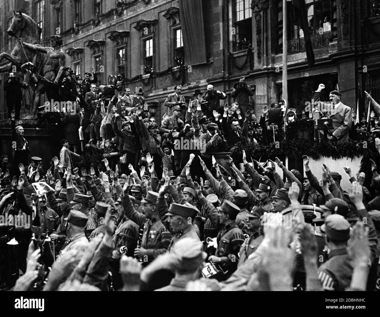 "En su primer año en el cargo, el NSDAP transformó el día del Trabajo en "Tag der nationalen Arbeit" (día Nacional del Trabajo) y lo convirtió en un acto de propaganda. En relación con la Volksgemeinschaft, los jóvenes de Hitler y el BDM se centran a menudo en este día. Aquí está Hitler frente a la Cancillería del Reich. Su audiencia lo saluda con entusiasmo con el saludo nazi." Foto de stock