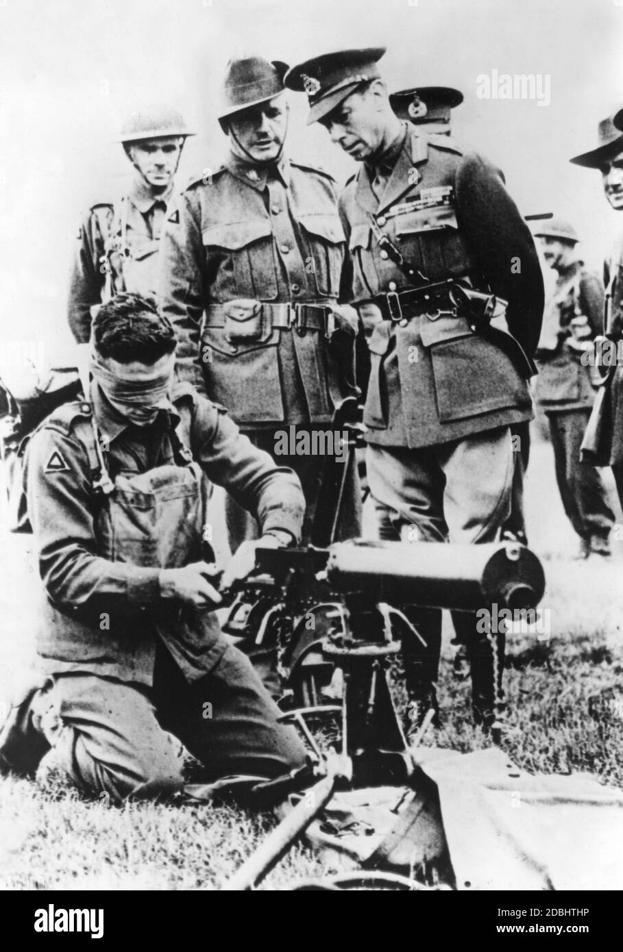Durante una visita a las tropas, el rey Jorge VI (a la derecha) observa a un soldado australiano montando su ametralladora vendada con los ojos. Foto de stock