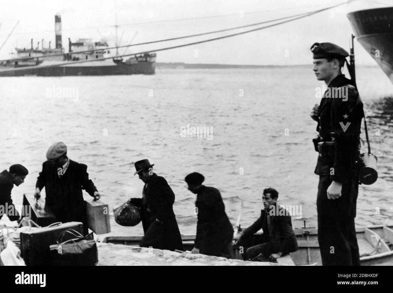 Un soldado alemán está de guardia en el Mar Mediterráneo en el puerto de una ciudad en el sur de Francia. Delante de él los pescadores están trabajando en su barco. Foto de stock
