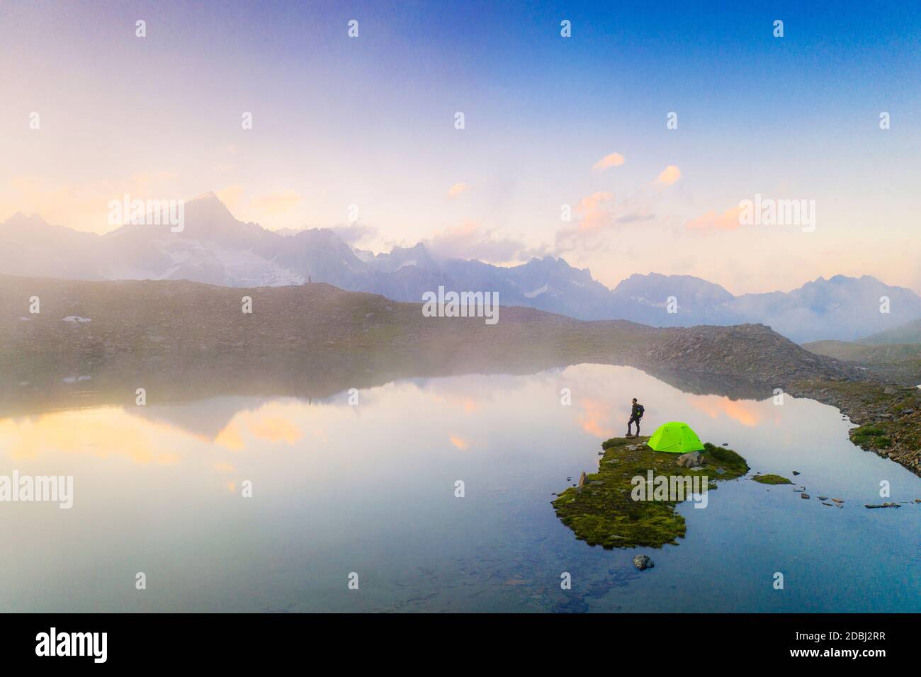 Hombre de excursionistas con carpa admirando un amanecer brumoso sobre las montañas desde el lago Obere Schwarziseeli, Paso Furka, Cantón Uri, Suiza, Europa Foto de stock