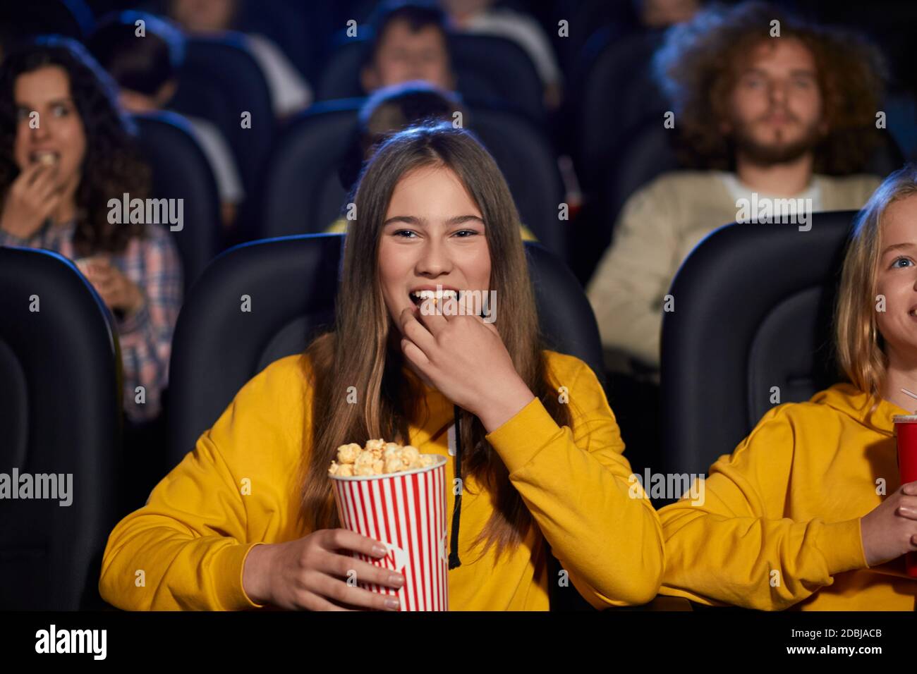 Enfoque selectivo de niña viendo películas en el cine, comiendo palomitas y riendo. Alegre mujer caucásica adolescente vestido suéter amarillo disfrutando de la película con amigos. Concepto de entretenimiento Fotografía de stock - Enfoque selectivo de niña viendo películas en el cine, comiendo palomitas y riendo. Alegre mujer caucásica adolescente vestido suéter amarillo disfrutando de la película con amigos. Concepto de entretenimiento Fotografía de stock -