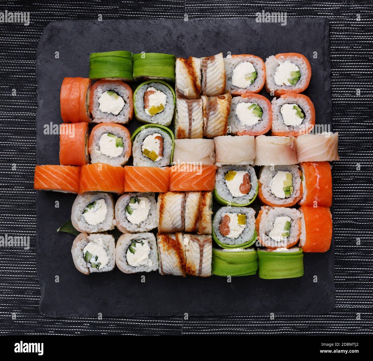 Sushi japonés. Varios tipos de roles en la placa sobre fondo de piedra. Vista superior, plano. Foto de stock