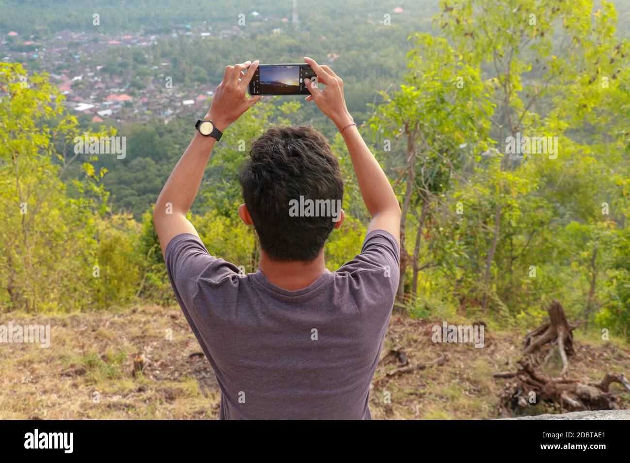El hombre fotografió montañas en el smartphone. Un joven toma fotos de un volcán con un teléfono móvil. Fotografías de adolescentes indonesios durante los soles Foto de stock