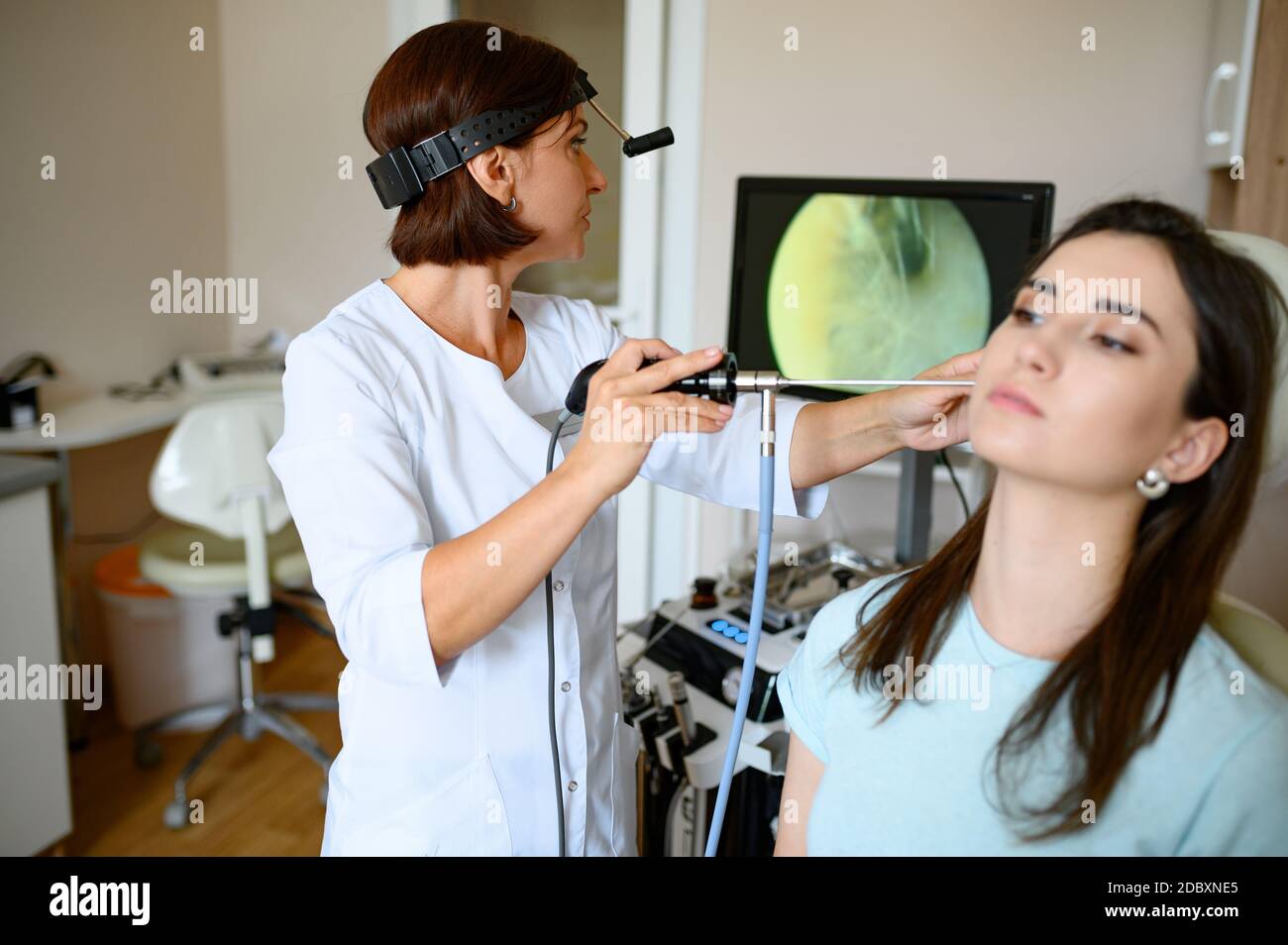 Joven mujer caucásica atractiva que recibe un examen médico del oído en una  clínica moderna. Profesional femenino que examina el oído del paciente,  usando un otoscopio, en el consultorio del médico Fotografía