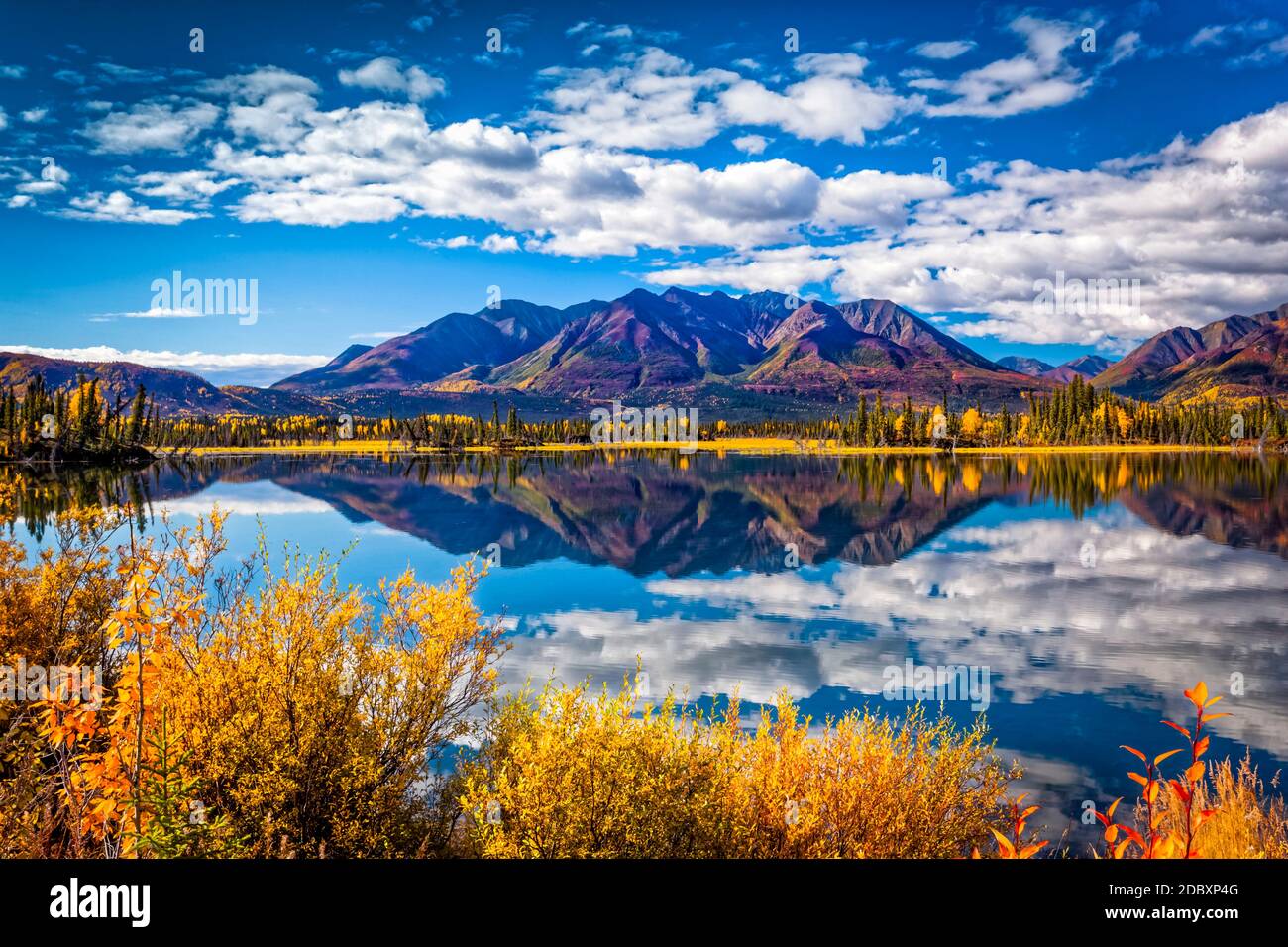 La cadena montañosa se refleja en el lago Mentasta con follaje de color caída bajo el cielo azul, Tok corte de la autopista Glenn, centro-sur de Alaska en otoño; Foto de stock